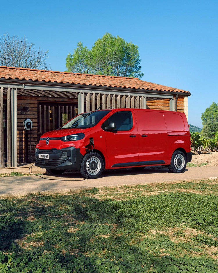 Seitenansicht eines roten Citroën ë-Jumpy beim Laden vor einem Gebäude, zeigt modernes Elektro-Design, Alltagstauglichkeit, Konnektivität und professionelles Auftreten.