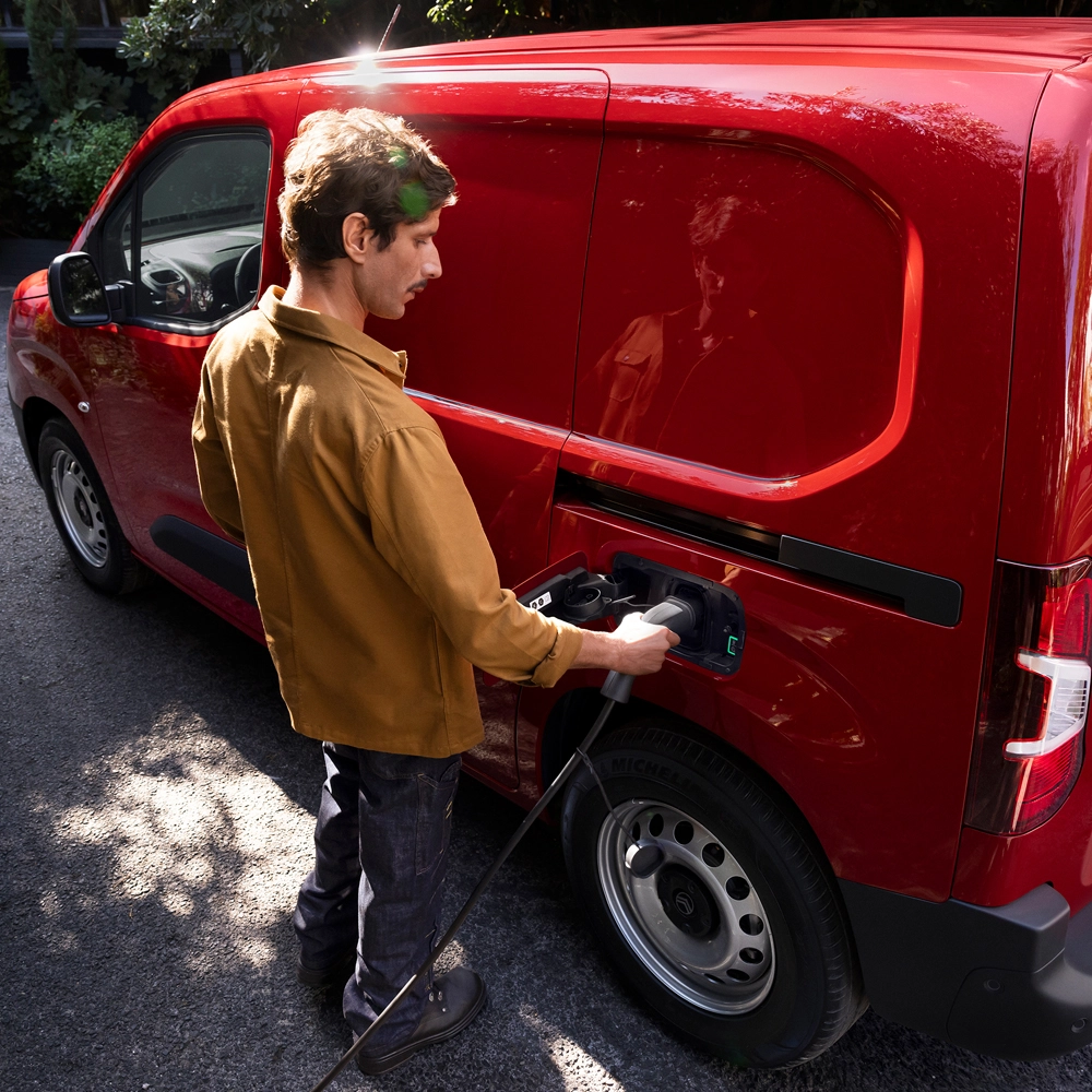 Seitenansicht (Dreiviertel-Perspektive) eines Citroën ë‑Berlingo Kastenwagen beim Laden; zeigt modernes Elektro-Design, Alltagstauglichkeit, Konnektivität und eine souveräne Präsenz.