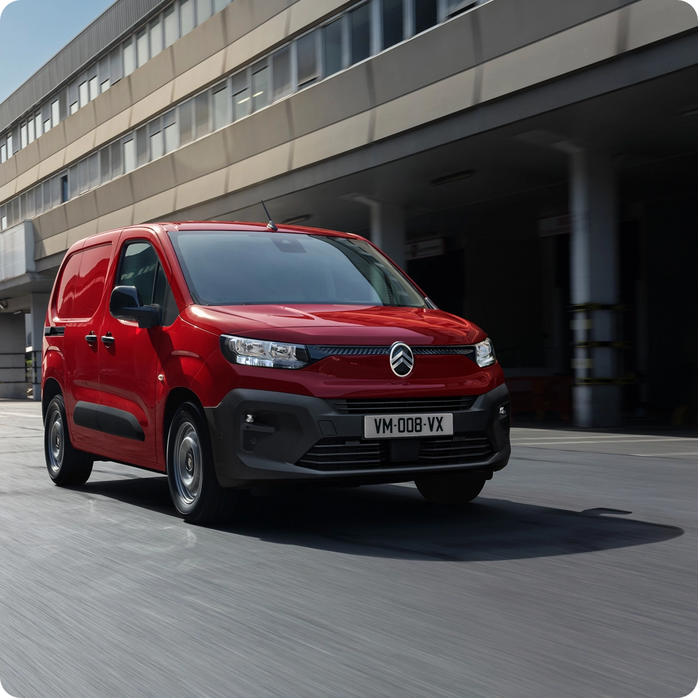 Front three-quarter view of a red Citroën van driving in an urban environment, highlighting safety and driving comfort features.