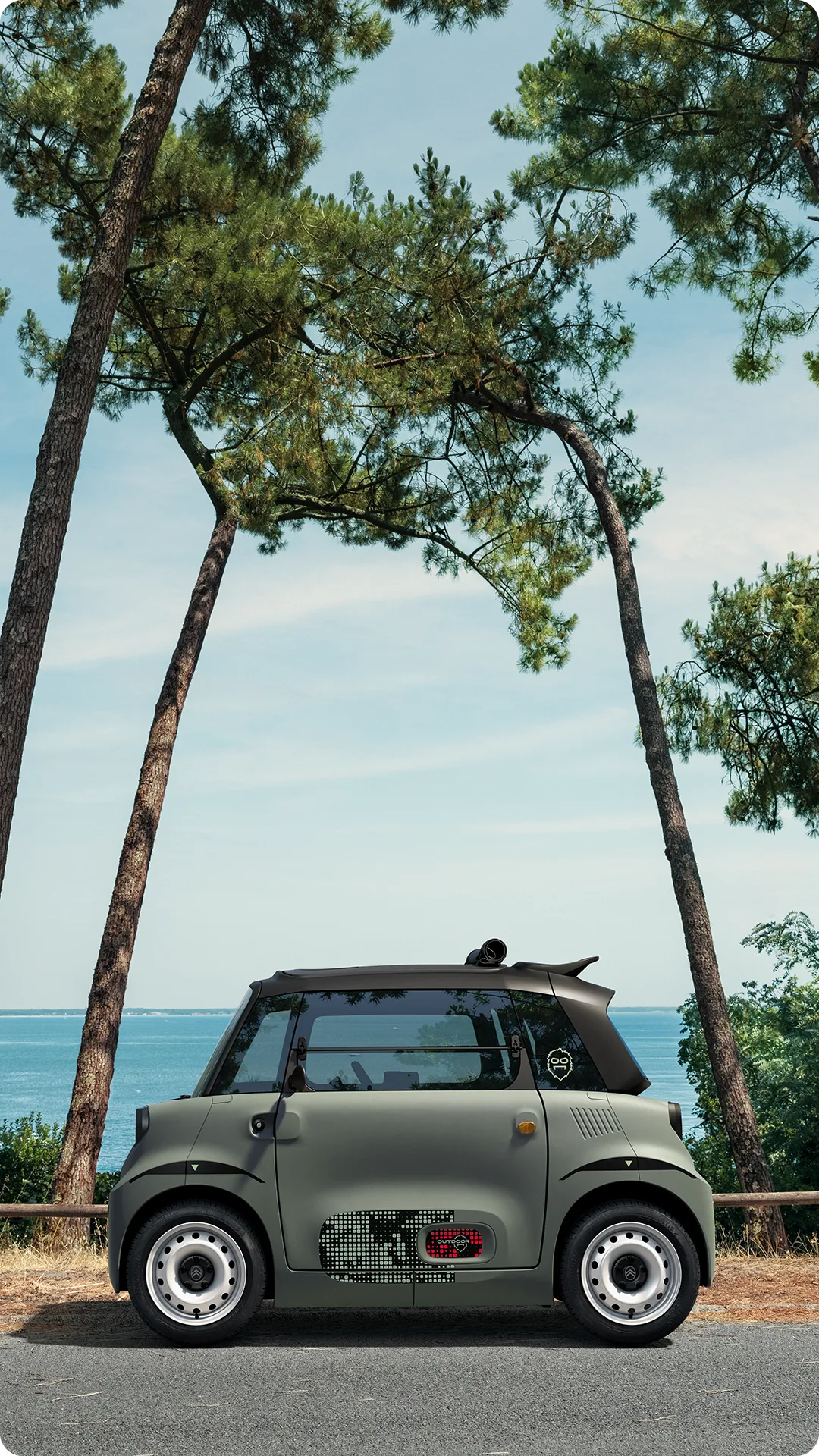 Seitenansicht des Citroën Ami Outdoor mit geöffnetem Dach zeigt das elektrische Stadtfahrzeug an der Küste für Freizeitmobilität