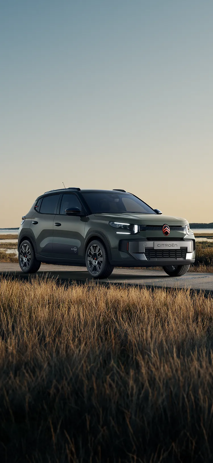 Front-Dreiviertelansicht des Citroën ë-C3 Outdoor mit LED-Lichtsignatur zeigt den Advanced Comfort SUV neben einer Küsten-Feuchtlandschaft