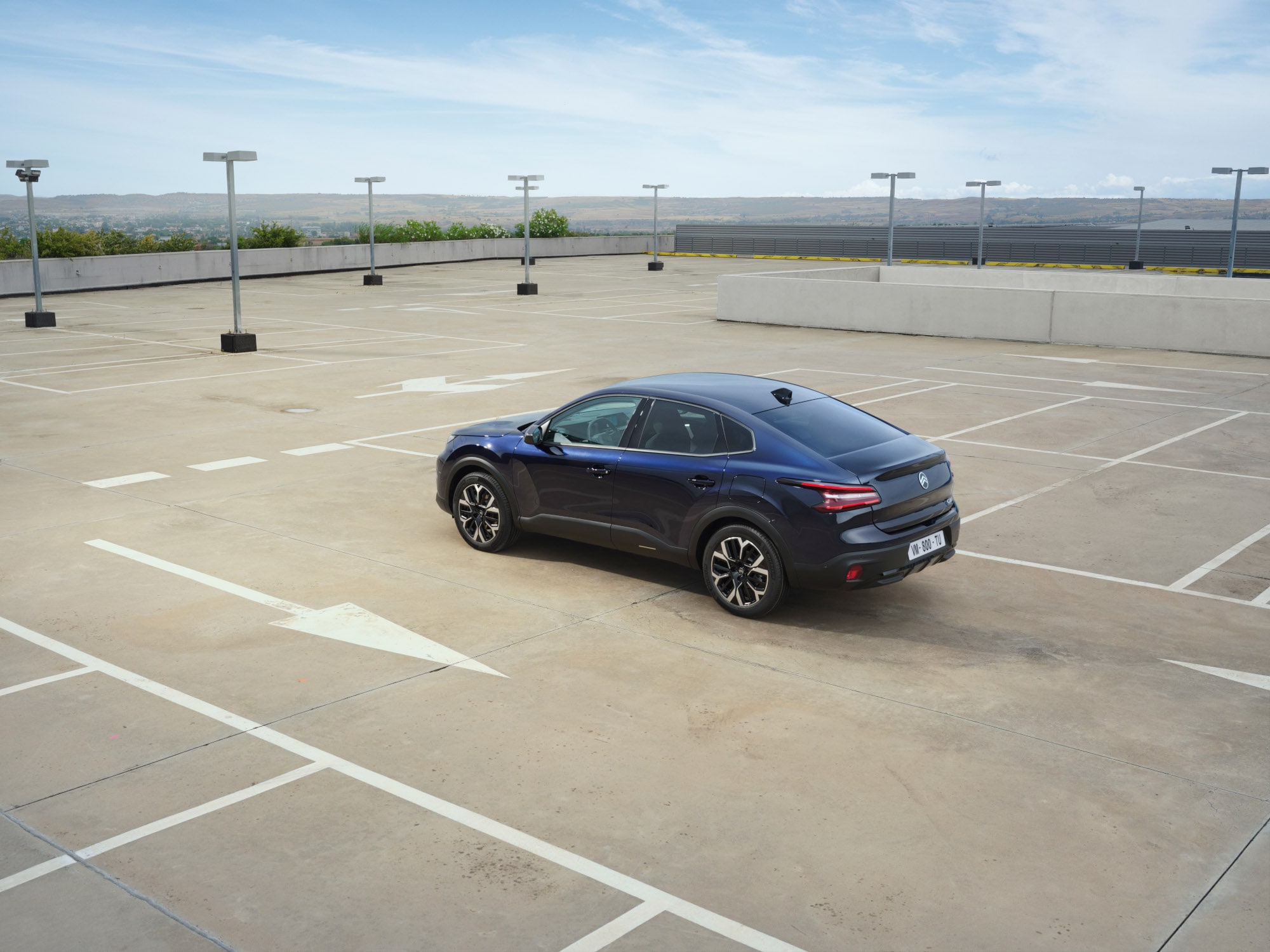 Dreiviertel-Heckansicht des Citroën C4 X auf offenem Dachparkplatz zeigt elegante Fastback-Linien für erschwingliche Mobilität