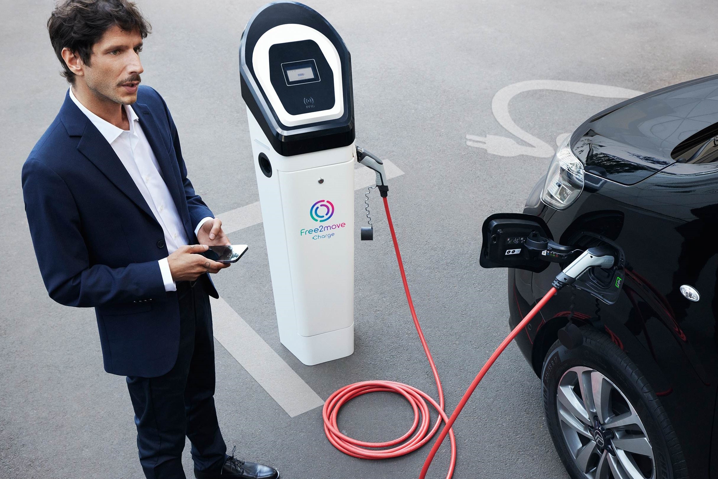 Elektrofahrzeug lädt an öffentlicher Ladestation während eine Smartphone-App das Laden mit Free2move Charge verwaltet